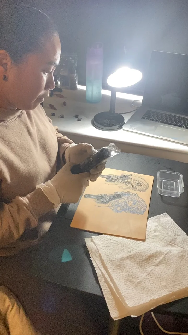 Nat holding a tattoo machine over a practice sheet